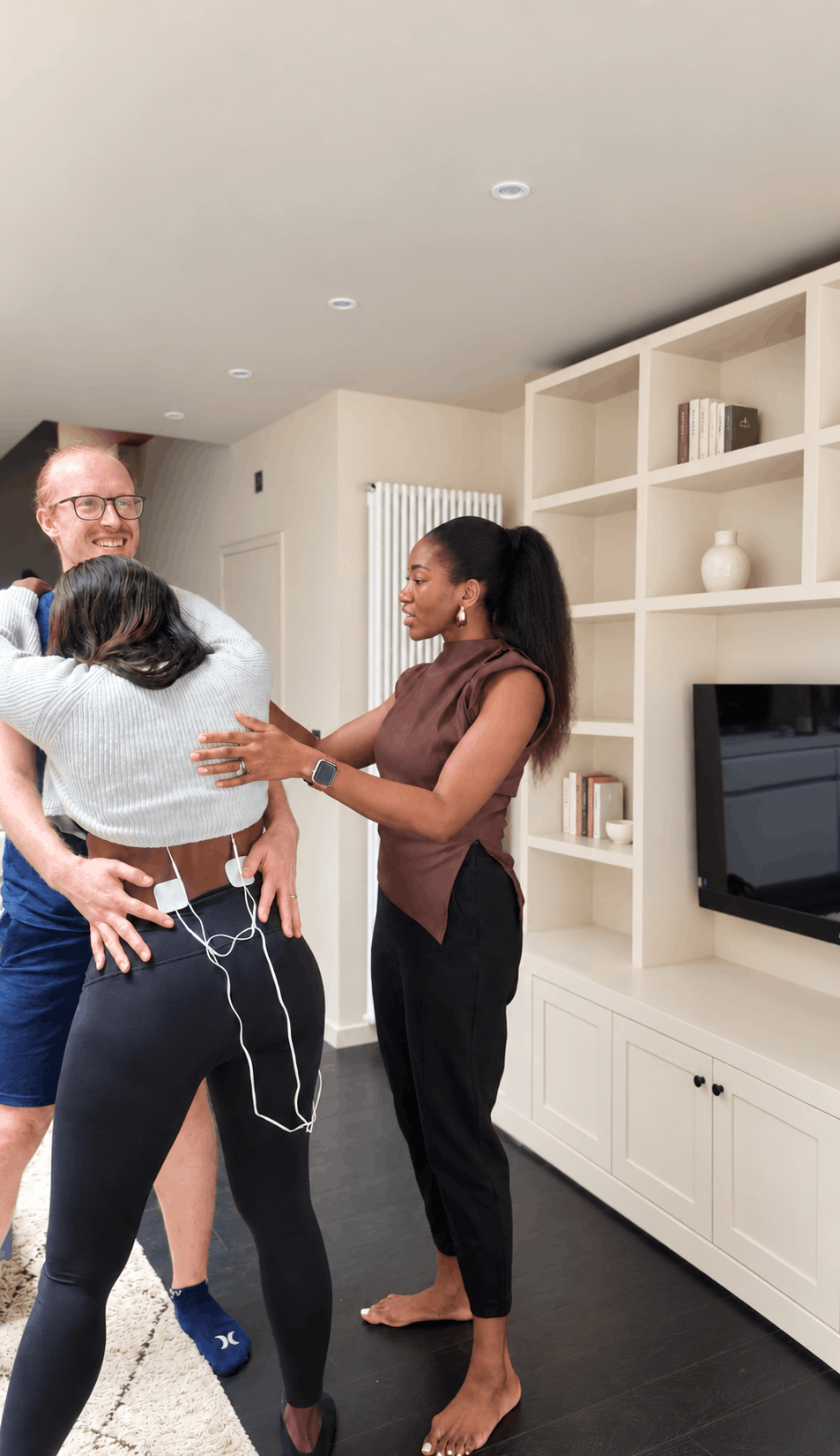 Steph guiding a partner’s hands onto a labouring person’s lower back during support at home, with a TENS machine in place.