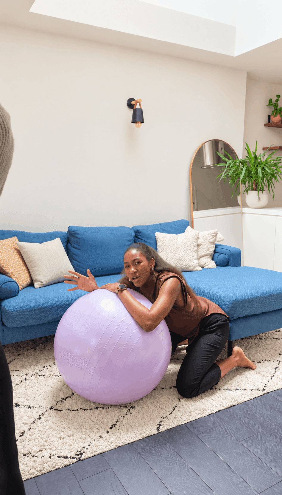 Steph kneeling beside a lilac birth ball in a living room, demonstrating a labour position.