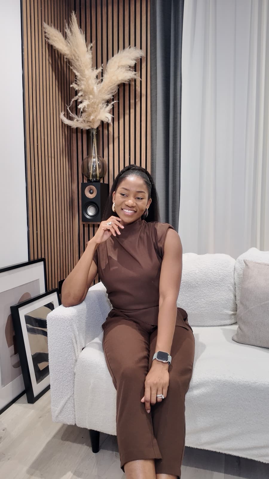 Steph Onye, The Doula Mamabear, seated on a white sofa in a brown outfit, smiling at the camera.